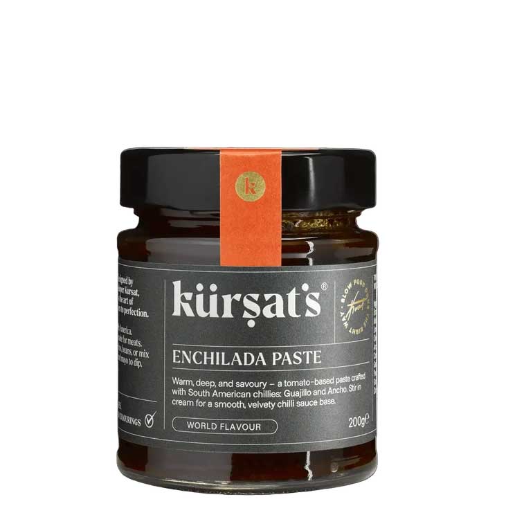 A glass jar of Kürşat's Enchilada Paste with a black lid and a vertical orange paper band around the neck, on a plain white background.