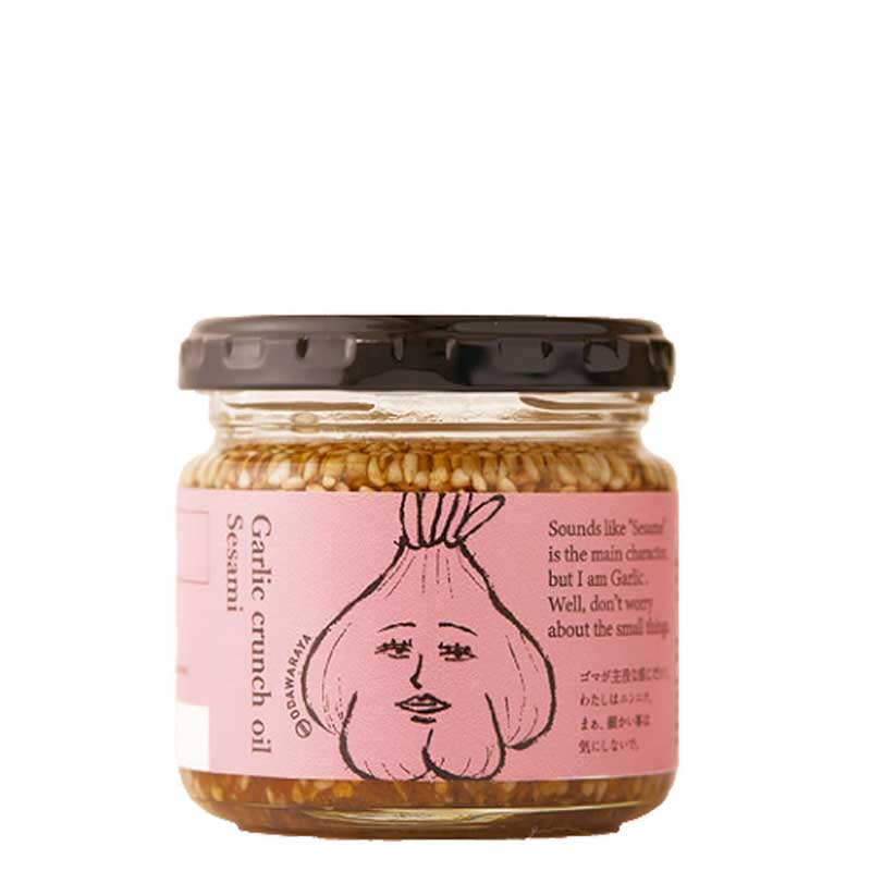 A glass jar of Odawaraya Garlic Crunch Oil with Sesame with a pink label featuring a cartoon garlic character and a black lid, set against a plain white background.