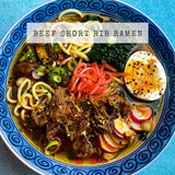 Recipe for Beef Short Rib Japanese Ramen showing a broth in a blue bowl with shredded beef, egg, noodles and pickled ginger.