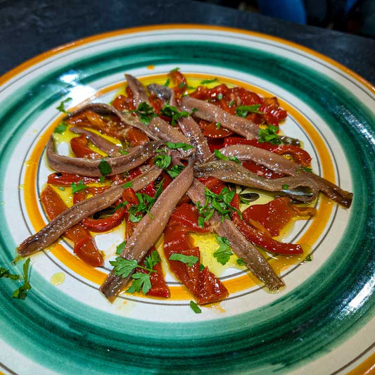 Cantabrian Anchovies with Sweet Red Peppers, olive oil and parsley on a green and orange plate