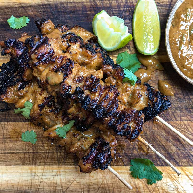 Picture of chicken satay skewers made with Jimmy's sate on wooden board with lime wedges