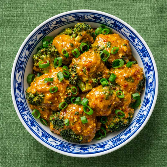 Recipe picture for Roni B's Kitchen Bang Bang Broccoli, showing roasted broccoli florets coated in a delicious sauce topped with spring onions.