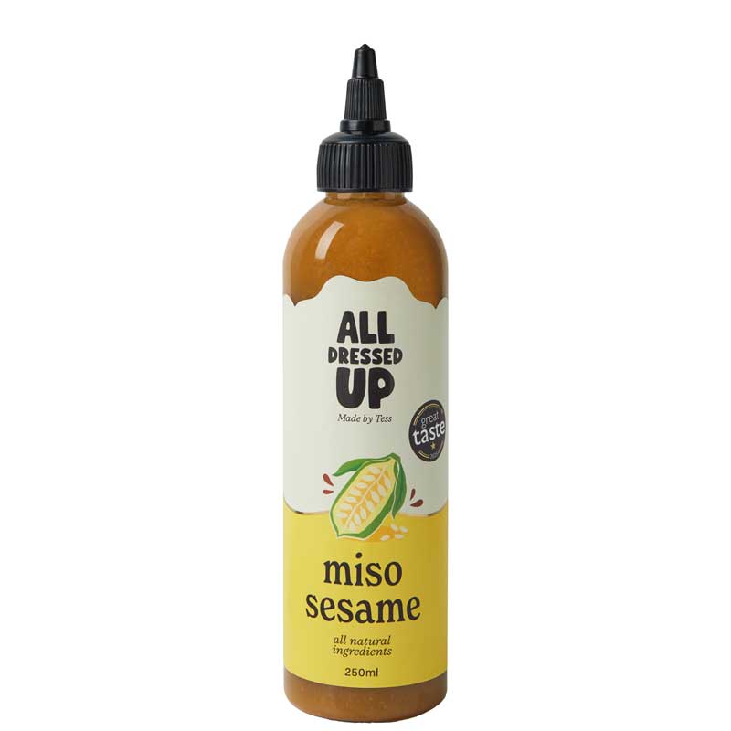 A 250ml squeeze bottle of All Dressed Up Miso Sesame dressing, featuring a black cap, amber-brown liquid inside, and a cream and yellow label with a sesame illustration.