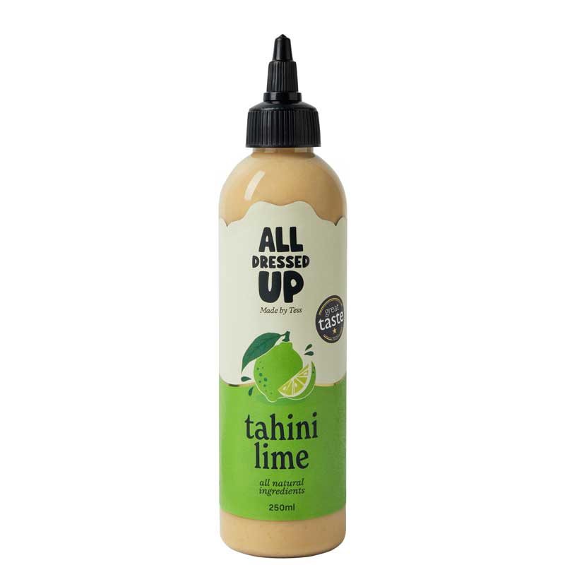 A 250ml squeeze bottle of All Dressed Up Tahini Lime dressing, featuring a beige-colored sauce inside, a black cap, and a label with green and white sections and a lime illustration.