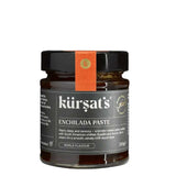A glass jar of Kürşat's Enchilada Paste with a black lid and a vertical orange paper band around the neck, on a plain white background.