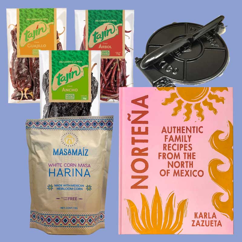 Gift box collection of Tajin seasoning packets, dried chilies, a masa harina package, and a book titled 'Norteña' on a blue background plus a cast iron taco press.